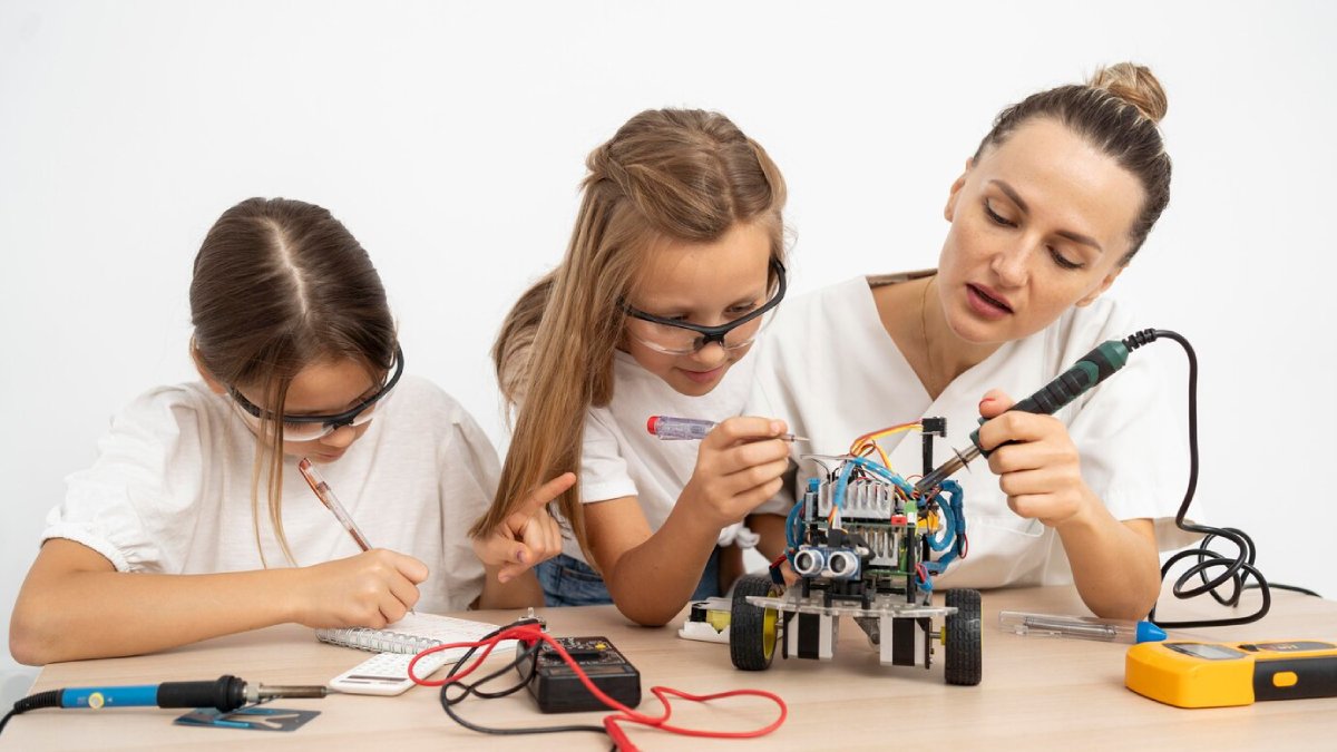 A woman and two girls building a robot, using various tools on a table.