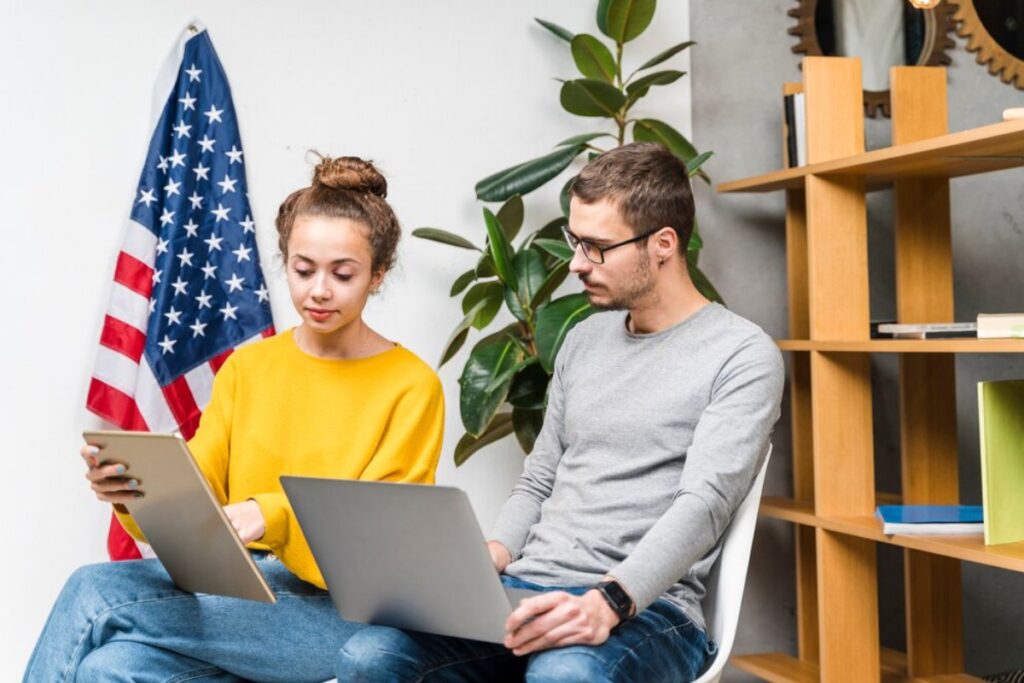 Two young adults using technology independently in a modern office, seated near a mounted American flag.